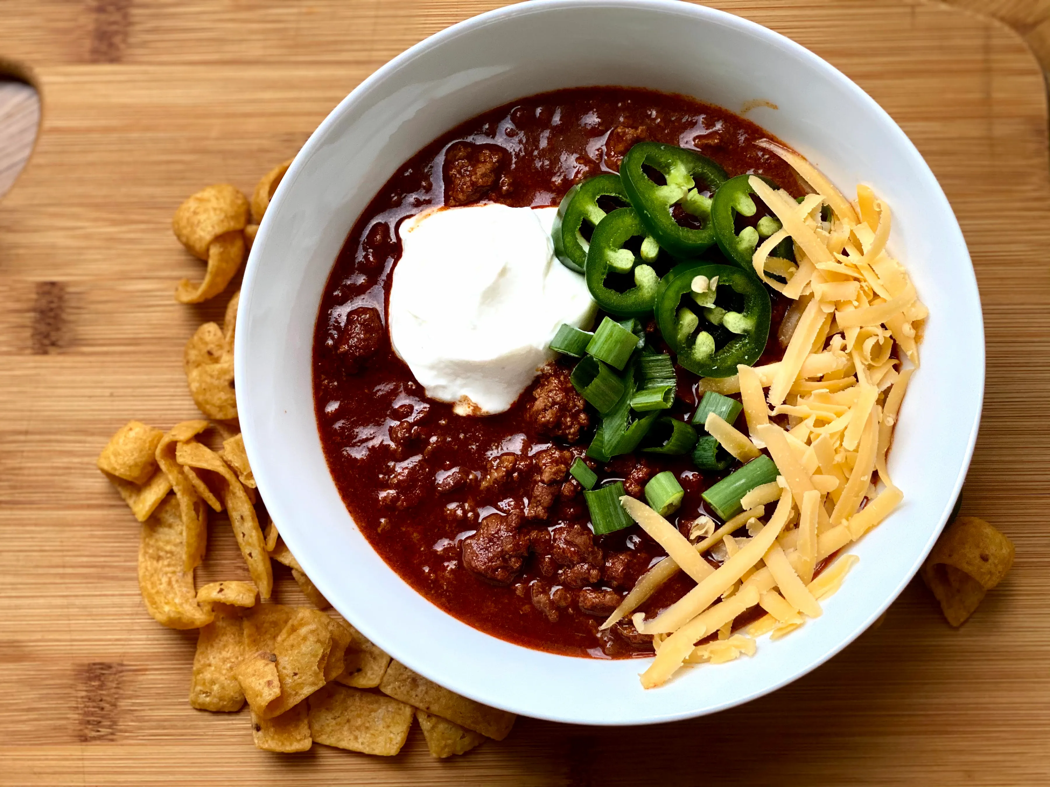 A finished bowl of Pecos Red Chili with sour cream, cheese, jalapeño, and green onions